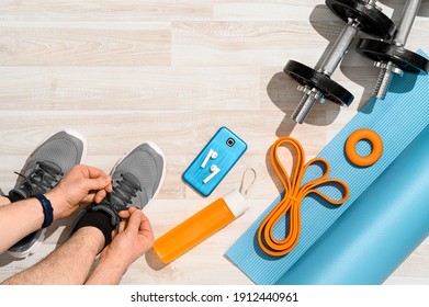 Workout at home concept. Overhead view of a man tying sport shoes with fitness equipment and smartphone on wooden floor. Morning training, sunlight. Place for text, top view. - Powered by Shutterstock