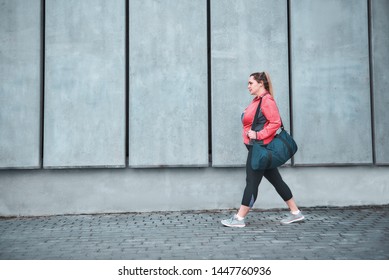 Workout is over. Back view of plus size woman in sport clothes carrying her bag and going home after exercises outdoors. Sport concept. Fatty women