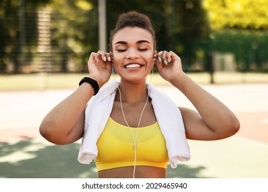 Workout Playlist. Portrait of satisfied fit African American woman wearing putting on earphones before training outdoors, exercising at public park, enjoying favorite song with closed eyes - Powered by Shutterstock