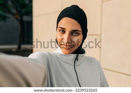 Workout selfies. Sporty Muslim woman looking at the camera while taking a selfie outdoors. Young woman with a hijab taking a break from exercising in the morning.
