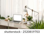 Workplace with blank laptop, lamp and green plants near window in office