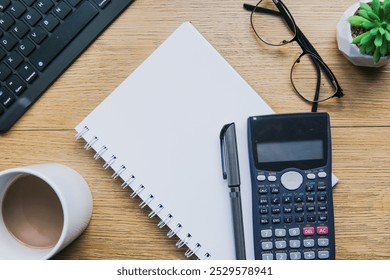 Workplace with blank open note, glasses, pen, calculator, a cup of hot coffee milk, keyboard and small plant on wood table background. Business-finance or education concept with copy space.
