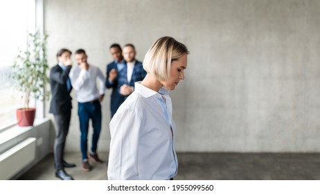 Workplace Bullying And Sexism. Male Colleagues Whispering Behind Back Of Unhappy Business Lady In Office. Victimization At Work. Female Discrimination Corporate Problem. Selective Focus, Panorama