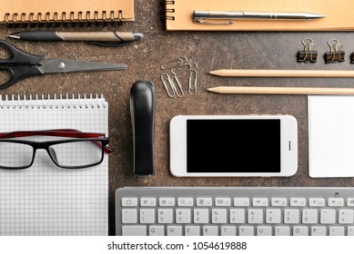 Workplace composition with computer keyboard, smartphone and stationery on table
