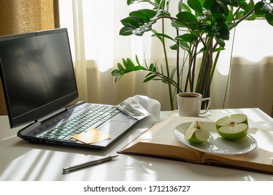 A workplace with a computer, an open book, an apple, a medical mask and a cup of coffee. Home office, remote work, distance education concept. Horizontal orientation, selective focus.