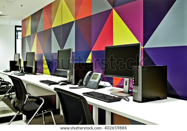 Workplace with computers, chairs and tables including telephones in front of a colorful wall design art