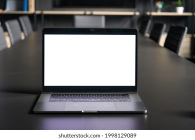 Workplace In Conference Room With Laptop Pc Computer On Desk With Blank Empty Mockup Screen For Advertising Standing In Dark Modern Contemporary Office. No People. Business Technologies Concept.