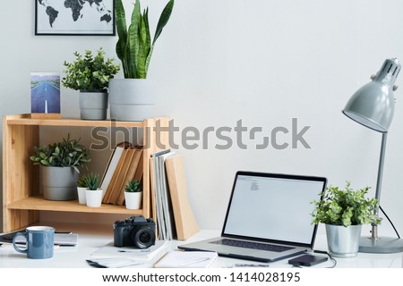 Workplace of contemporary stock photographer with photocamera, laptop, drink in mug and table lamp in office