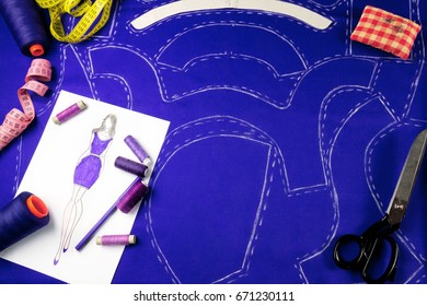 Workplace of a dressmaker:  pattern, scissors, needles, measuring tape,textile, sewing spools, sketch and pencil.