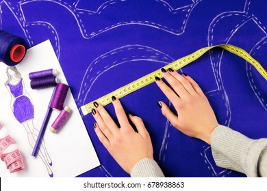 Workplace of a dressmaker: scissors, pattern, needles, textile, sewing spools and measure tape. Girl measuring patterns with the measuring tape