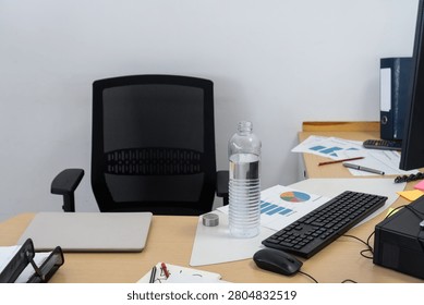 Workplace with an empty chair, desk, computer, water, and business documents