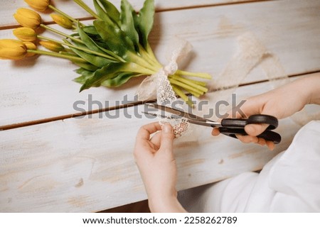 Workplace of a florist. Close-up of flowers in hand on a wooden background. A woman makes a bouquet of tulips and other flowers. Florist teacher at master classes or courses.