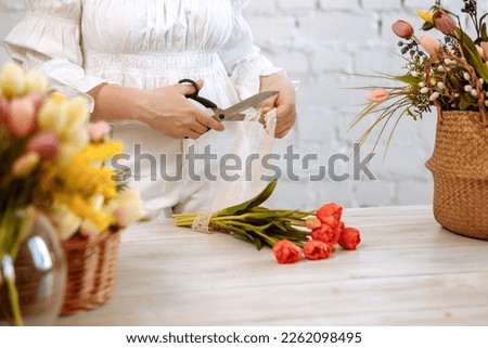 Workplace of a florist. Close-up of flowers in hand on a wooden background. A woman makes a bouquet of tulips and other flowers. Florist teacher at master classes or courses.