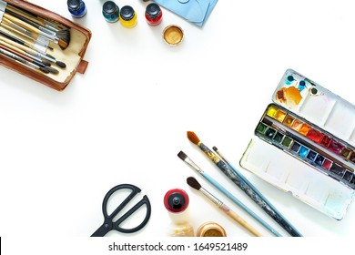 Workplace Of Freelance Artist Top View On White Background. Flat Lay Composition With Copy Space. Paints, Brushes And Other Various Equipment