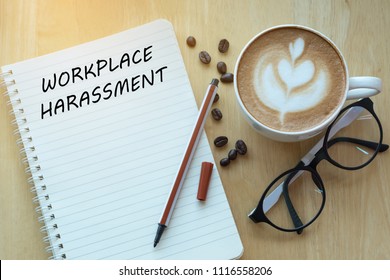 Workplace harassment concept on notebook with glasses, pencil and coffee cup on wooden table. Business concept.