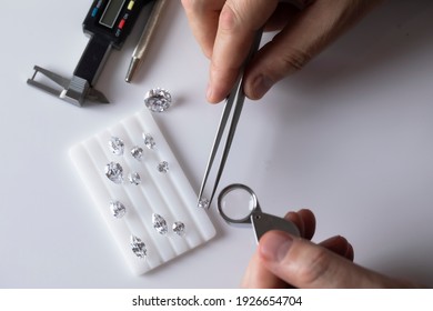 Workplace of jewellery buyer. Top view of hands with tools and diamonds of different cut on white platform for color determination.