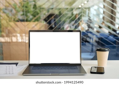 Workplace in morning with laptop on desk with blank empty mockup screen for advertising standing in modern contemporary office with coffee, paper documents and cellphone. No people. Business concept.