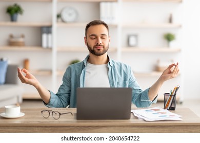 Workplace stress management. Calm Caucasian man meditating with closed eyes in front of laptop pc at home office. Young male freelancer feeling peaceful and balanced, doing yoga at his desk - Powered by Shutterstock