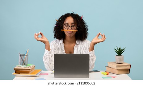 Workplace Stress Management. Silly Black Woman With Pencils In Her Hair Meditating In Front Of Laptop On Blue Background, Panorama. Young Female Student Feeling Peaceful And Balanced, Doing Yoga