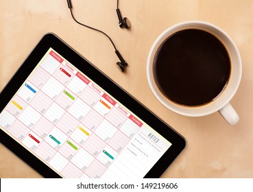 Workplace With Tablet Pc Showing Calendar And A Cup Of Coffee On A Wooden Work Table Close-up