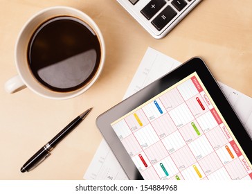 Workplace with tablet pc showing calendar and a cup of coffee on a wooden work table close-up - Powered by Shutterstock