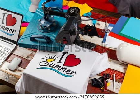 Workplace top view with heat transfer shirt press to manufacture custom DIY design shirts with notebook computer and cutting machine. Startup fashion designer production concept.