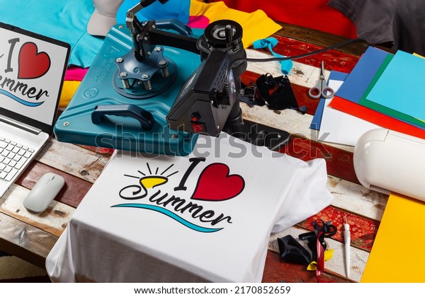 Workplace top view\
with heat transfer shirt press to manufacture custom DIY design\
shirts with notebook computer and cutting machine. Startup fashion\
designer production\
concept.