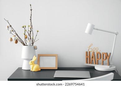 Workplace with tree branches and Easter eggs in vase near grey wall - Powered by Shutterstock