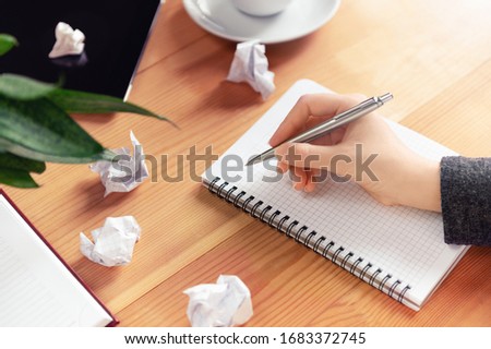 Workplace of writer, rewriter. Female hand holding pen and writing in notepad. Crumpled paper and creature process. Business planning and brainstorming concept