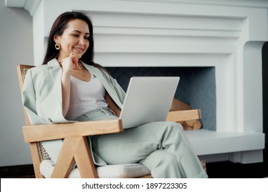 works online on a laptop computer, prints text to a project partner. The student manager is sitting on a chair of a young woman of Caucasian appearance. a favorite work, a comfortable business suit