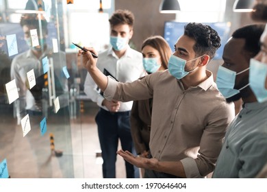 Workshop And Brainstorming Concept. Diverse group of multicultural business people in face masks having meeting, using sticky paper post-it notes on glass wall or window to share ideas and thinking - Powered by Shutterstock