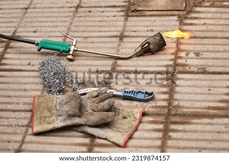 Workshop floor, protective gloves and tools, including a lit blowtorch, throwing fire. Composition without people with copy space.