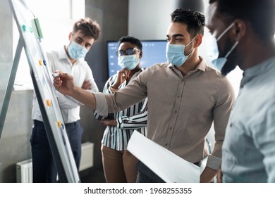 Workshop. Male Business Coach In Surgical Medical Face Mask Giving Flipchart Presentation, Arab Speaker Consulting And Training Diverse Multicultural Employees, Mentor Leader Explaining Graph Strategy