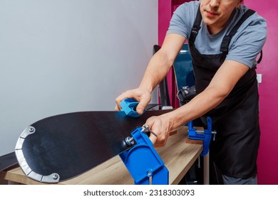 Workshop man preps skis and snowboards for winter by sharpening edges holding ski in vises - Powered by Shutterstock