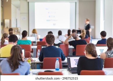 Workshop At University. Rear View Of Students Sitting And Listening In Lecture Hall Doing Practical Tasks On Their Laptops. Copy Space On White Screen.