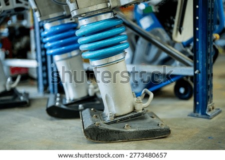Workshop view of large blue coil spring shock absorbers with bolted mounts and metal tubes for machine stability and maintenance business use now