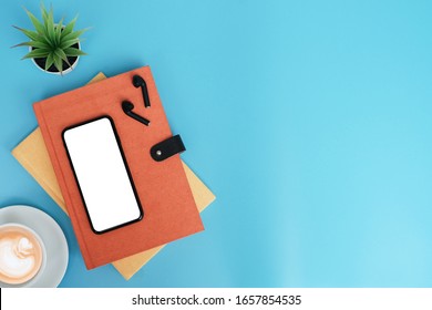 Workspace back to school and education concept on blue table desk with blank screen phone and stack of book, earphone, green plant and coffee cup, flat lay, Top view with copy space