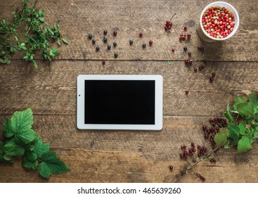 Workspace. Composition with tablet pc and bilberries, cowberries, red currant with leaves in the old wooden impressive boards. Natural light shadows