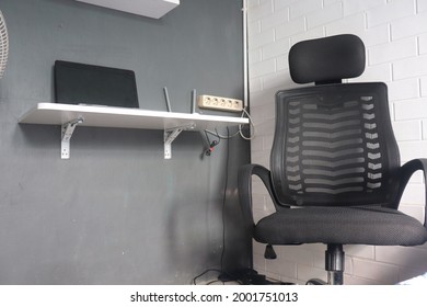 A Workspace Consisting Of A Messy Desk, Chair And Laptop And A Wall-mounted Shelf