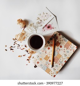 Workspace. Cup Of Black Coffee, Sketchbook, Pencil, Two Watercolor Cards And Beige Dried Roses Isolated On White Background. Overhead View. Flat Lay, Top View