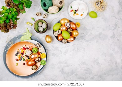 Workspace With Easter Decoration. Painted Eggs In Trays, Candy, Flowers With Copy Space. Holiday Background. Flat Lay, Top View