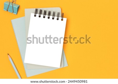 Workspace with empty notepad mockup and mint colored stationery on a yellow background. Office supplies.