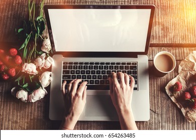 Workspace With Girl's Hands, Laptop Computer, Bouquet Of Peonies Flowers, Coffee, Strawberries, Smartphone On Rough Wooden Table. Freelancer Working In Outdoor Park. Top View Office Desk. Flat Lay