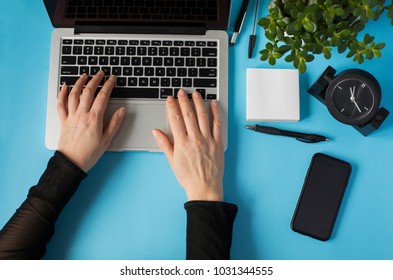 Workspace with girl's hands, laptop, pen, papers and flower in the pot on blue background.Top view office desk. Flat lay, top view - Shutterstock ID 1031344555
