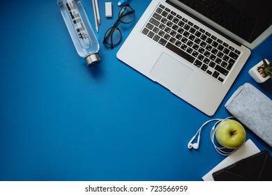 Workspace for healthy person with laptop, pencils, water, apple, phone, glasses, headphones on a blue background. Top view, flat lay, space for text - Powered by Shutterstock