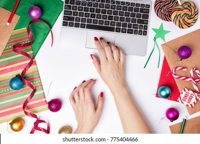 Workspace with laptop and wrapping paper. Flat Lay Christmas or Party Background with ribbons, candy canes, baubles, Star tag and decorations. Female hands typing - Powered by Shutterstock