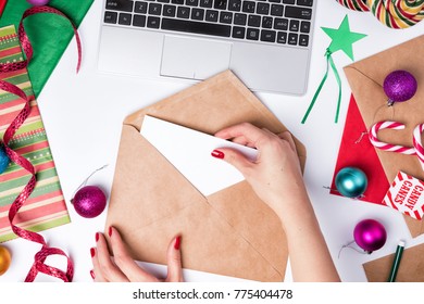 Workspace with laptop and wrapping paper. Flat Lay Christmas or Party Background with ribbons, candy canes, baubles, Star tag and decorations. Female hands holdings envelope  - Powered by Shutterstock