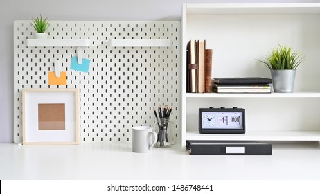 Workspace Pegboard And Shelves With Office Supplies On White Office Desk.