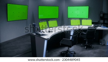 Workspace in security control center for monitoring CCTV cameras. Computer monitors on the table and big digital screens on the wall with chroma key showing surveillance cameras footage. Green screen.