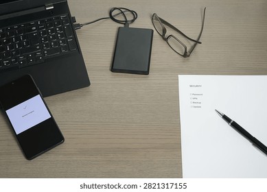 Workspace setup with a laptop, smartphone, external HDD, and a checklist for 